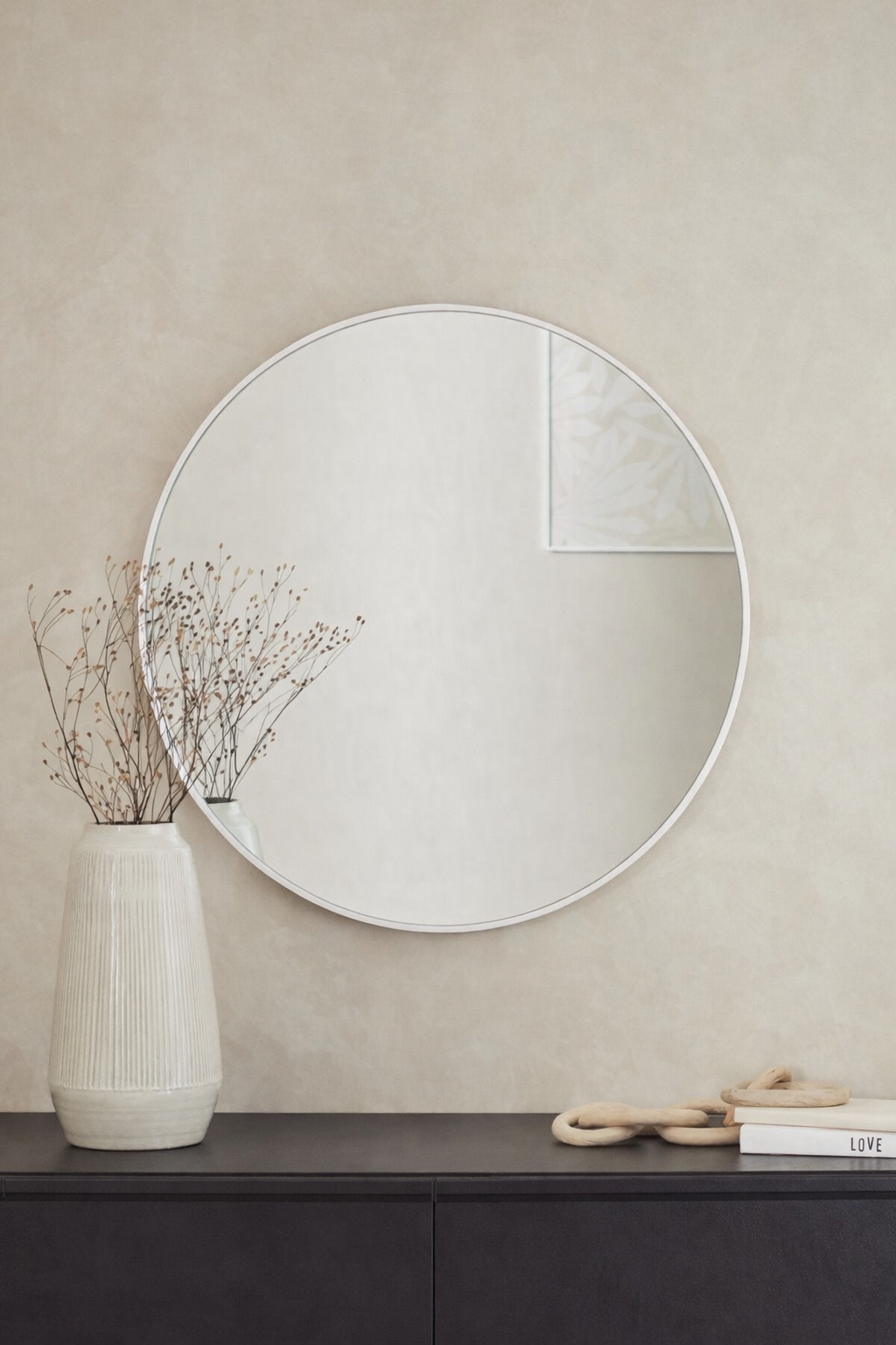 מראה עגולה מעוצבת עם מסגרת בהירה מעל שידה בעיצוב מינימליסטי